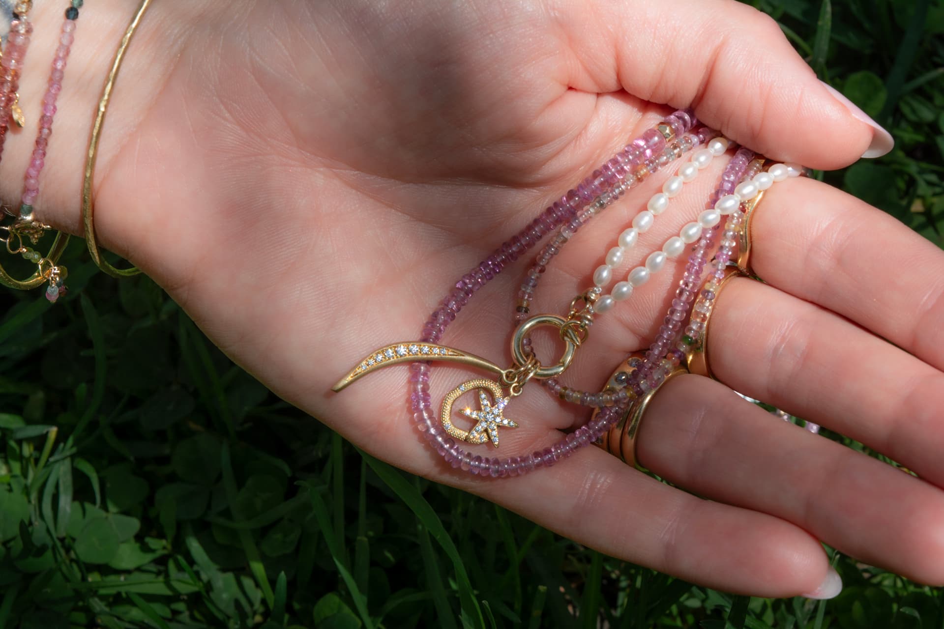 Pink gemstone strands with diamond charms held in the hand