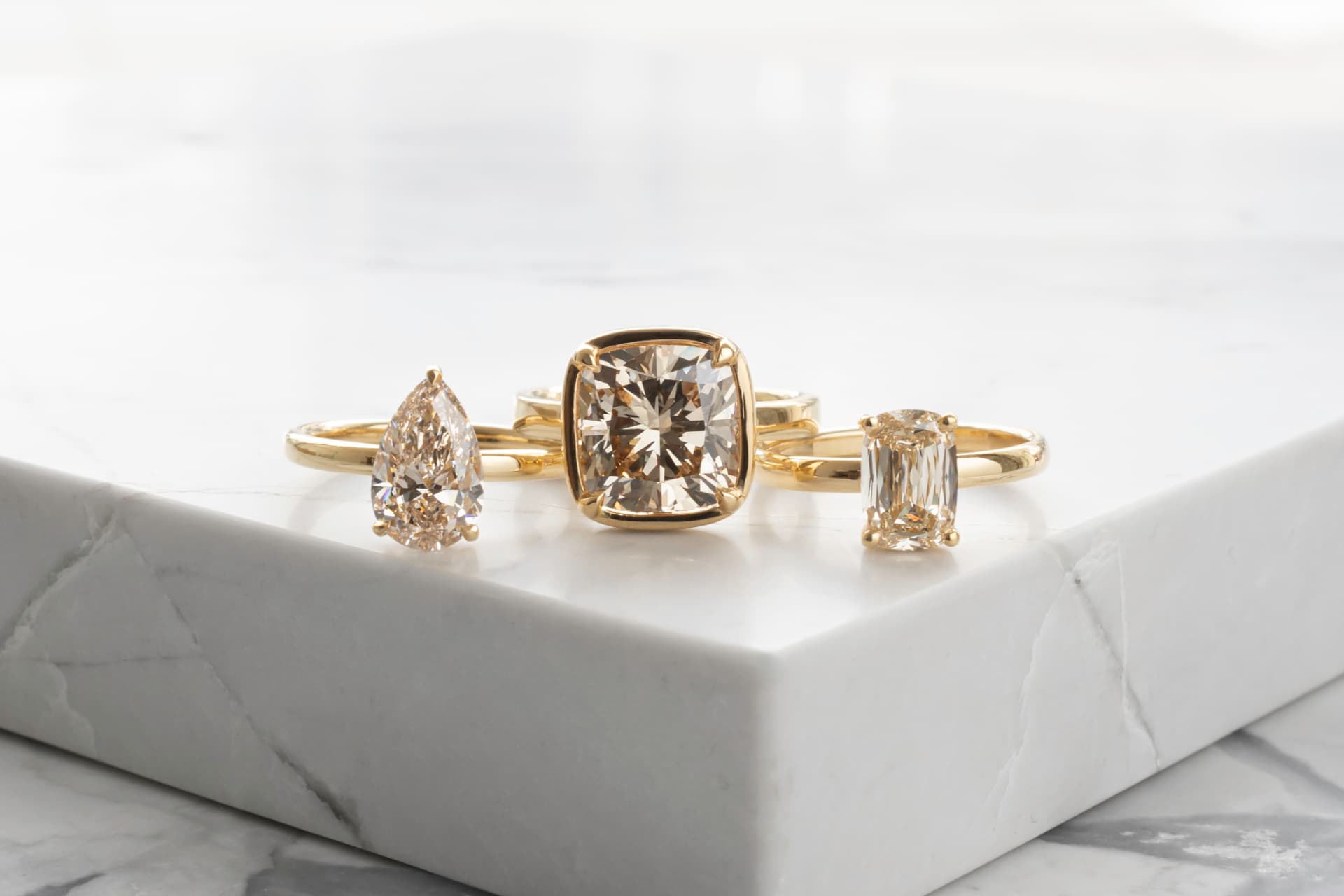 Three champagne diamond rings displayed on white stone